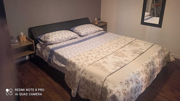 Un lit bien fait, avec une literie à motifs floraux, une table de chevet avec une lampe et un miroir accroché au mur.