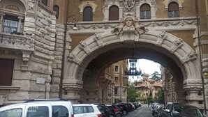 Un arc en pierre orné de sculptures complexes, qui mène à une rue bordée de voitures garées et de bâtiments historiques.