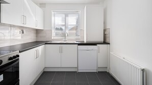 A modern kitchen with white cabinets, a black countertop, a dishwasher, and a window with blinds. - Stylish 4 bed 3 bath- Mill Hill (London)