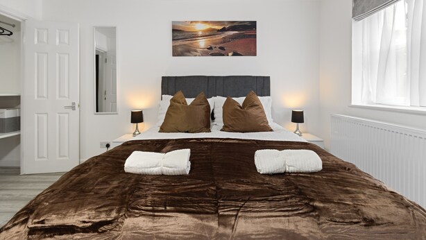 A bedroom with a large bed, two bedside tables with lamps, a painting of a sunset, and a window with curtains. - Stylish 4 bed 3 bath- Mill Hill (London)