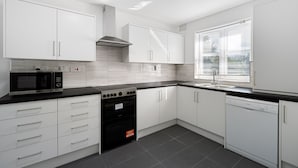 A modern kitchen with white cabinets, a black countertop, a built-in oven, and a dishwasher. - Stylish 4 bed 3 bath- Mill Hill (London)