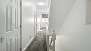 A hallway with white walls, a carpeted floor, and a staircase with a white railing. - Stylish 4 bed 3 bath- Mill Hill (London)