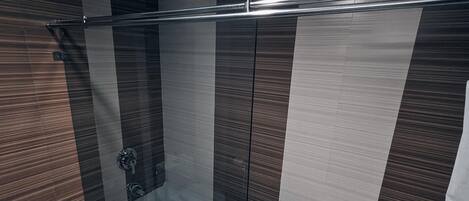 A modern bathroom with a glass shower enclosure, a metal towel rack, and a tiled floor.