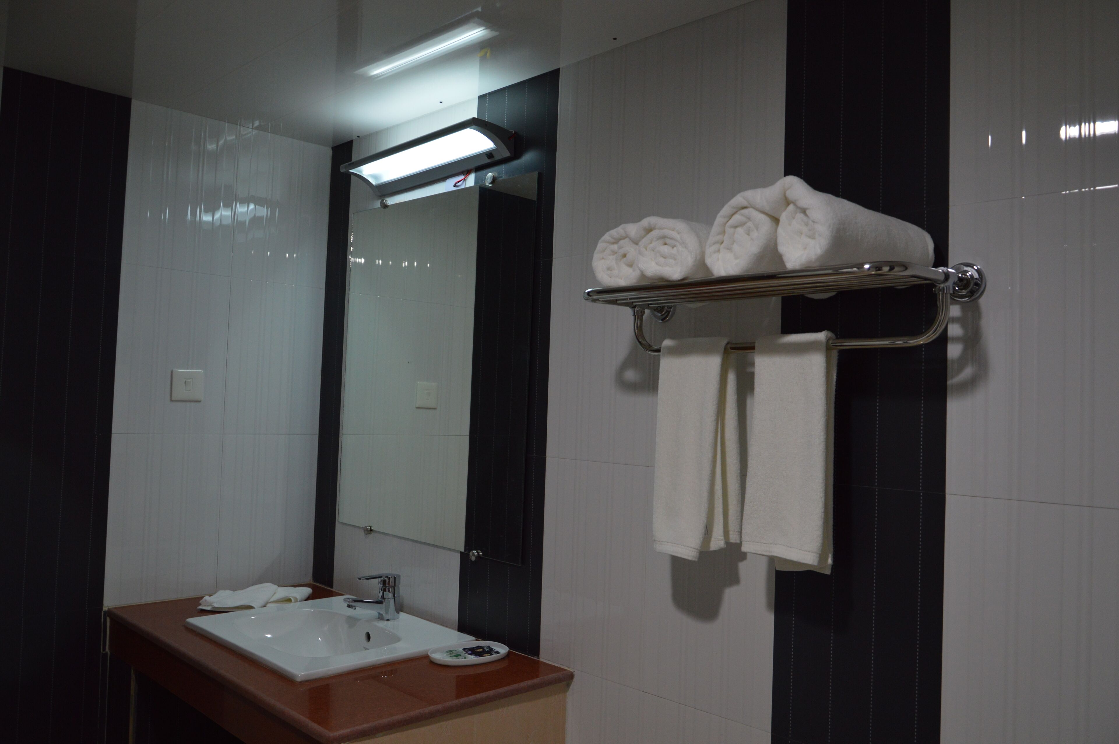 A modern bathroom with a white sink, mirror, and towel rack holding rolled towels.