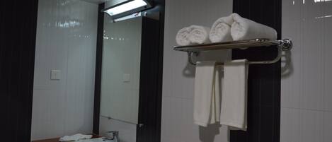 A modern bathroom with a white sink, mirror, and towel rack holding rolled towels.