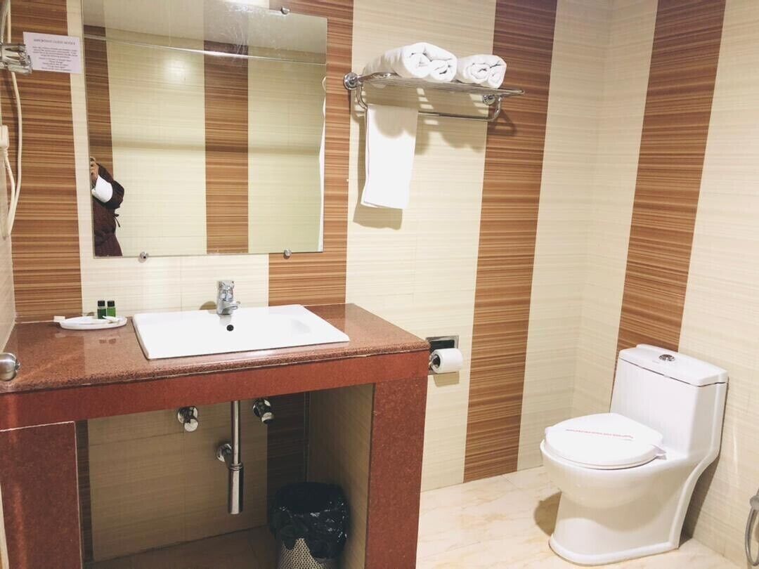 Een badkamer met een wastafel, spiegel, handdoekhouder, toilet en een prullenbak.