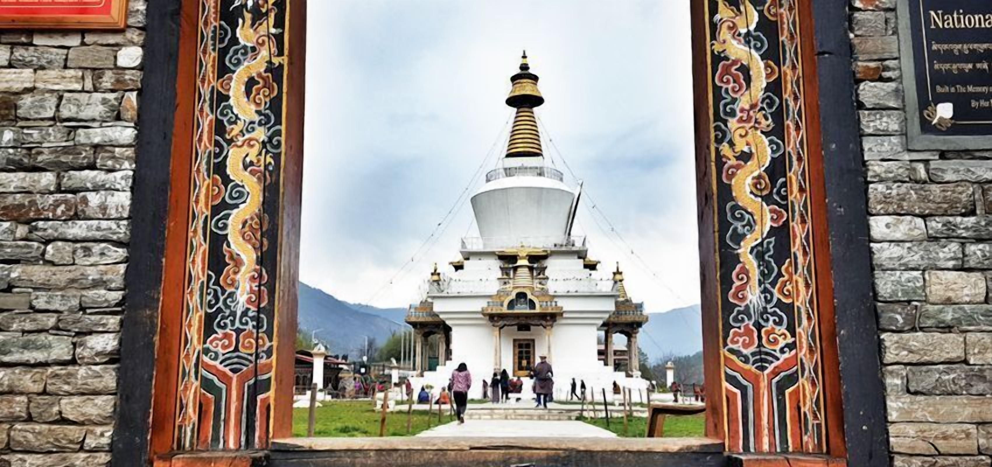 A traditional white stupa with a golden spire, surrounded by a stone wall and a decorative wooden frame.