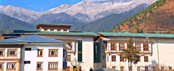 Un edificio tradizionale con tetto verde, pareti bianche e finestre decorate, sullo sfondo di montagne innevate.
