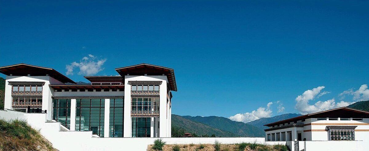 A modern building with large windows and a flat roof, set against a mountainous backdrop.