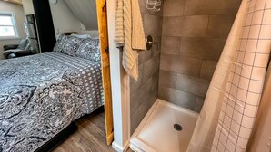 Ein Schlafzimmer mit einem gemusterten Bettbezug, einer Holztür und einem Duschbereich mit gefliestem Wand und Duschvorhang.