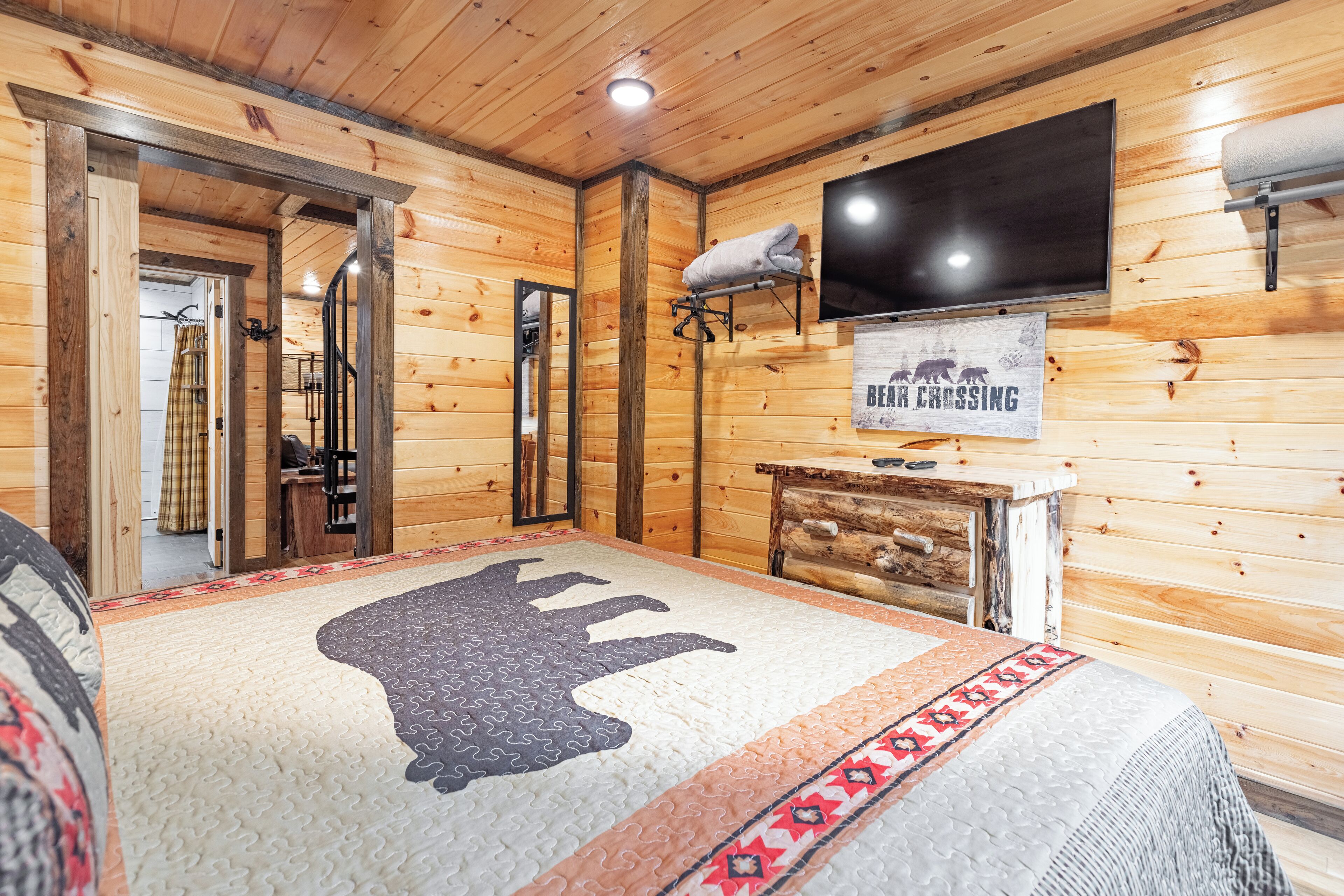 Een houten kamer met een bed, een tv aan de muur, een bordje met de tekst 'Bear Crossing' en een houten dressoir.