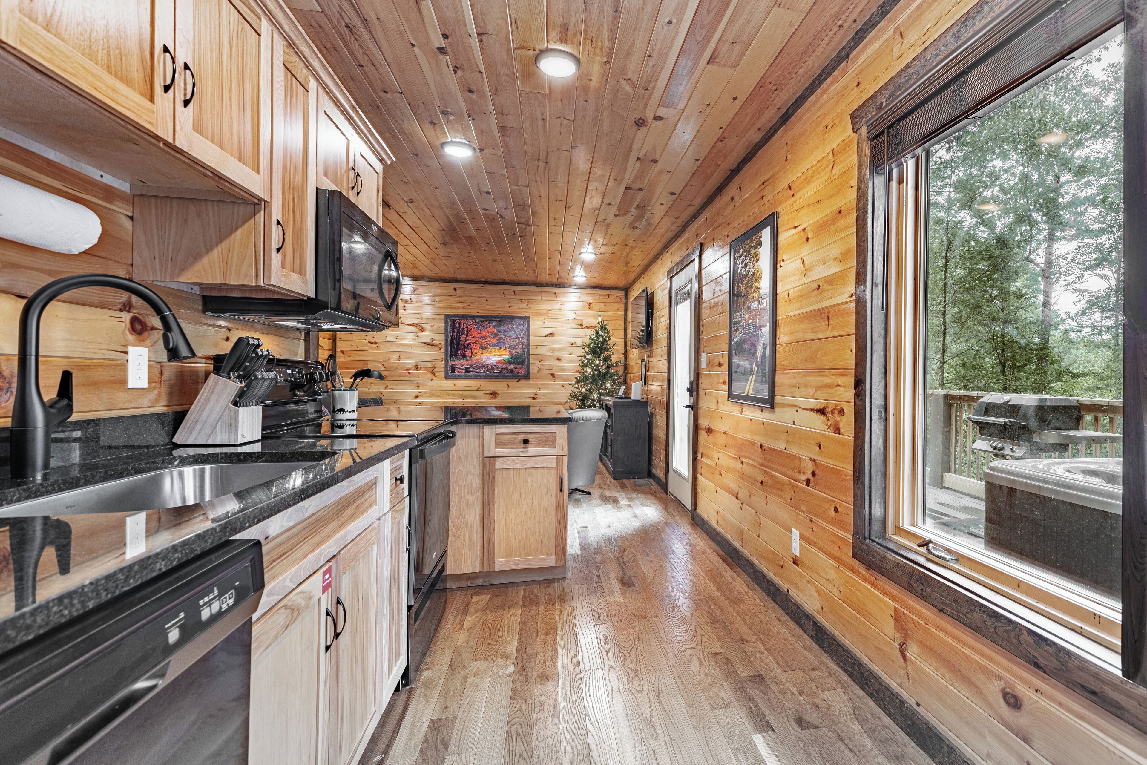 L’intérieur d’un chalet en bois comprend un coin cuisine, des placards en bois, un lave-vaisselle et de grandes fenêtres offrant une vue sur l’extérieur.
