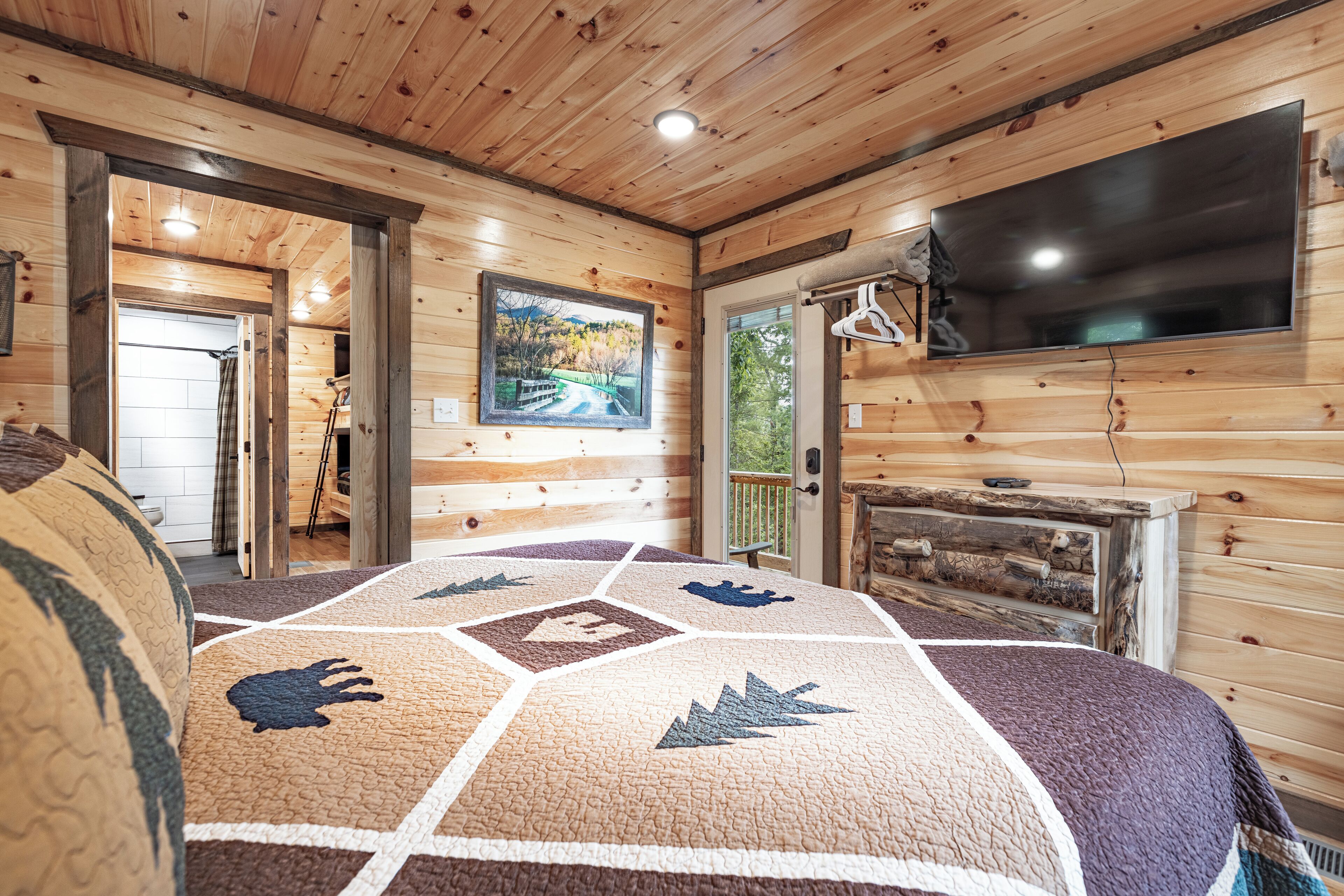 Une chambre dans un chalet en bois, avec un grand lit, un téléviseur fixé au mur et un tableau représentant un paysage.