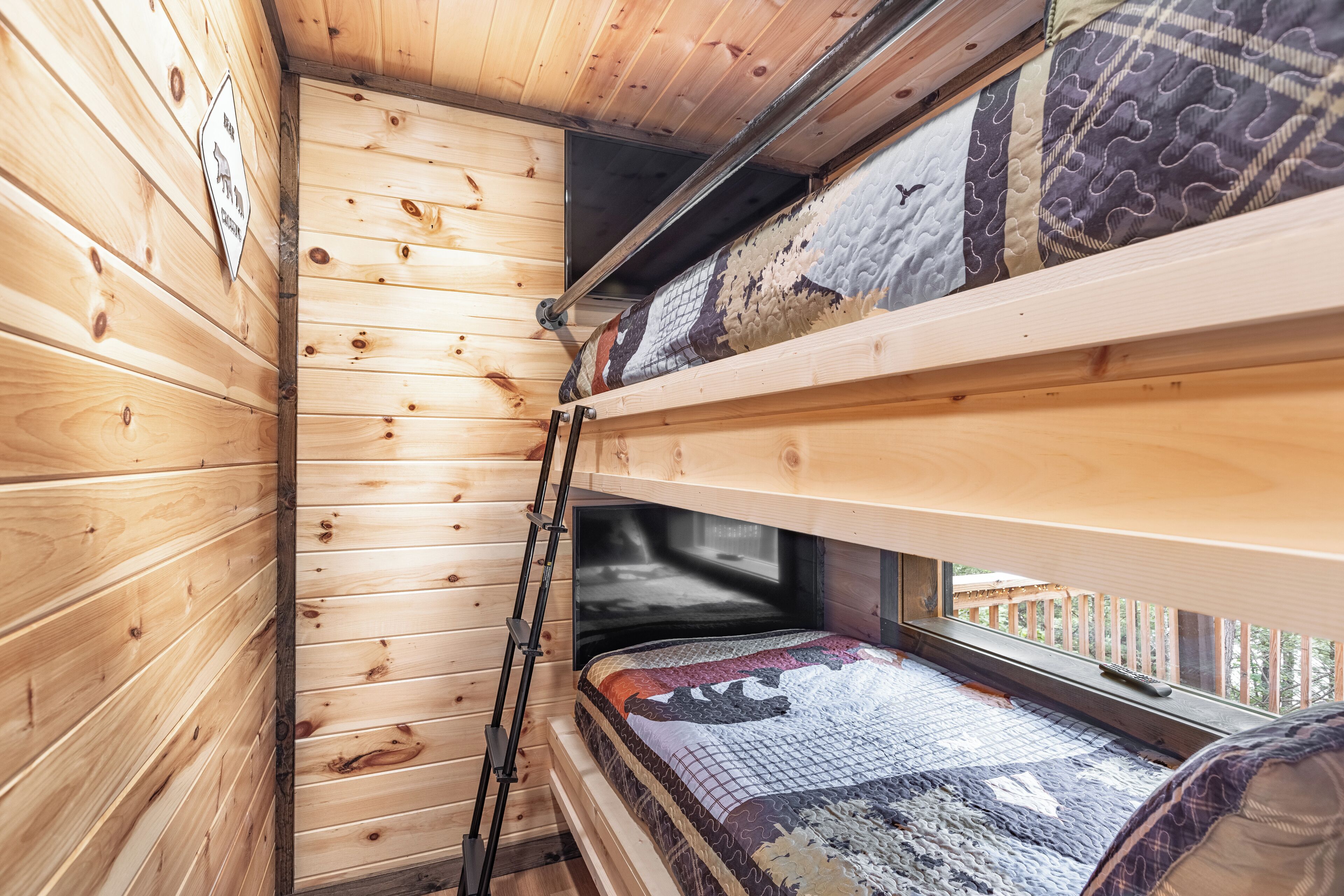 A cabin with wooden walls, a bunk bed, a ladder, and a window with a view.
