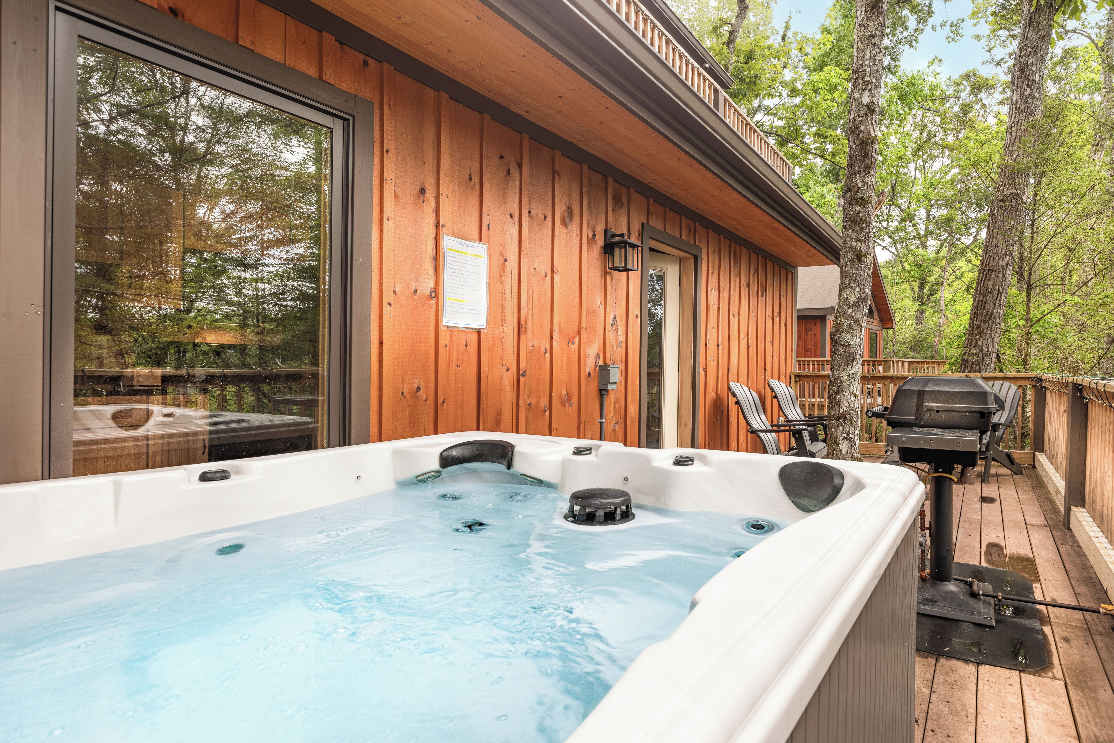 A wooden cabin with a hot tub, outdoor seating, and a deck surrounded by trees.