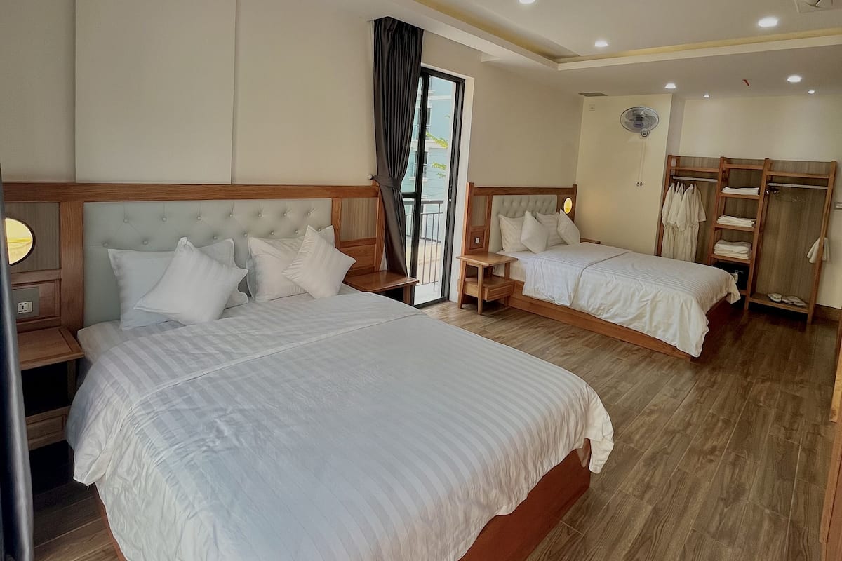 A hotel room with two beds, wooden flooring, a ceiling fan, and a window with curtains.