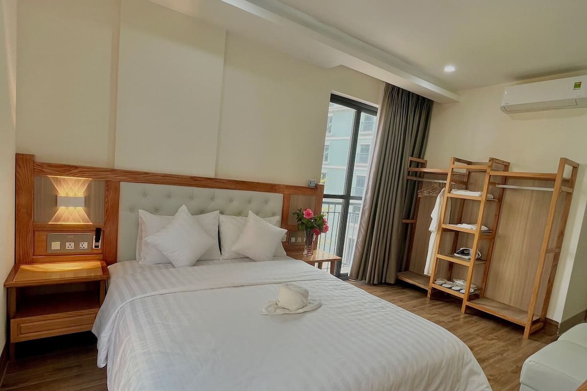A hotel room with a large bed, wooden nightstands, a wardrobe, and a window with curtains.