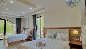 A hotel room with two beds, a wooden floor, a ceiling fan, and a view of greenery outside. - SK BOUTIEQUE HOTEL (Phu Quoc)