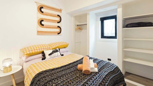 Een slaapkamer met een bed, nachtkastje, hanglamp, kast en raam.