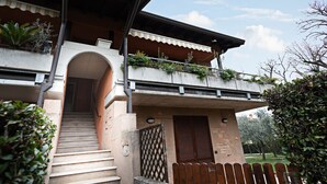 A two-story building with a staircase leading to an entrance, a balcony with plants, and a wooden fence.
