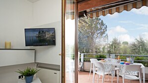 A balcony with a table set for dining, a television mounted on the wall, and a potted plant on a small table.