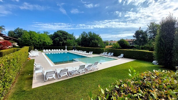 A rectangular swimming pool with a clear blue water surface, surrounded by white lounge chairs and a well-maintained lawn.