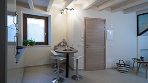 A compact kitchen with a dining area, a wooden door, and a window with blinds.
