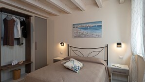 A bedroom with a bed, a painting of a beach scene, and two bedside tables with lamps.