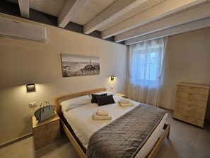 A bedroom with a bed, bedside tables, a dresser, a painting, and a window with curtains.