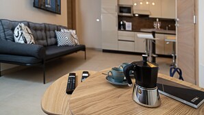 A modern living room with a sofa, remote controls, a coffee maker, and a dining table.