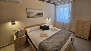 A bedroom with a bed, bedside tables, a dresser, a painting, and a window with curtains.
