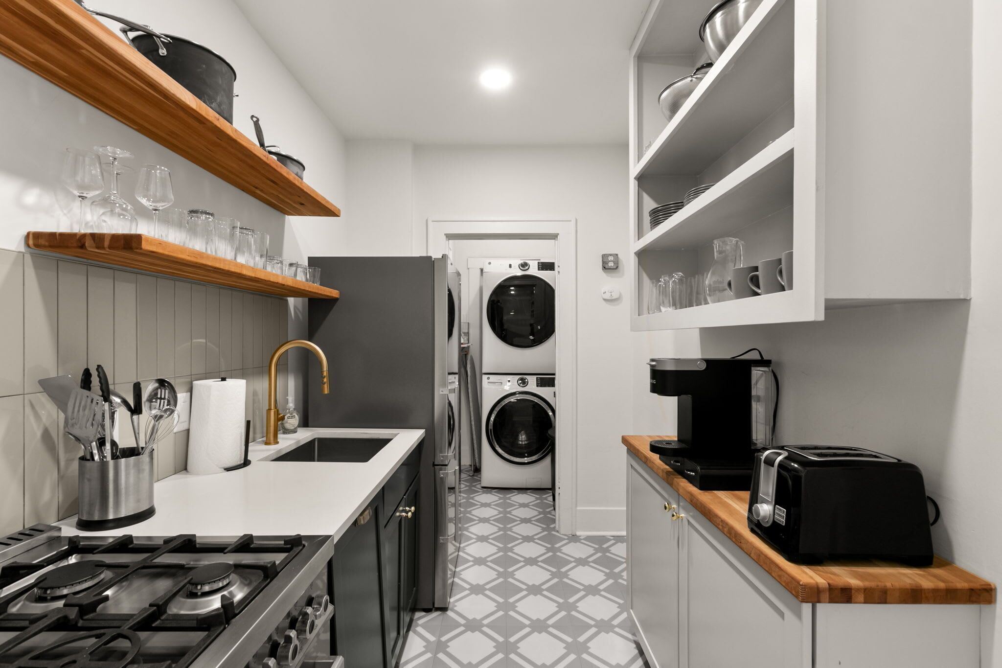 A compact kitchen with a gas stove, a sink, a washing machine, and a coffee maker.