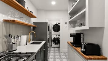 A compact kitchen with a gas stove, a sink, a washing machine, and a coffee maker.