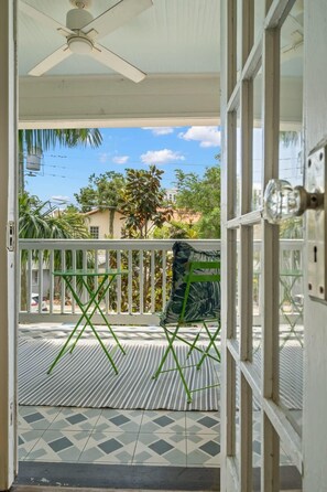 Une pièce dotée d’un ventilateur de plafond, offrant une vue sur l’extérieur, avec un balcon agrémenté d’une chaise verte et d’un tapis à motifs, ainsi qu’une porte avec un interrupteur.