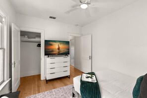 A bedroom with a bed, a dresser, a ceiling fan, and a painting of a sunset. - SoHo Siesta | Stunning SoHo Apt w/ Private Balcony (Tampa)