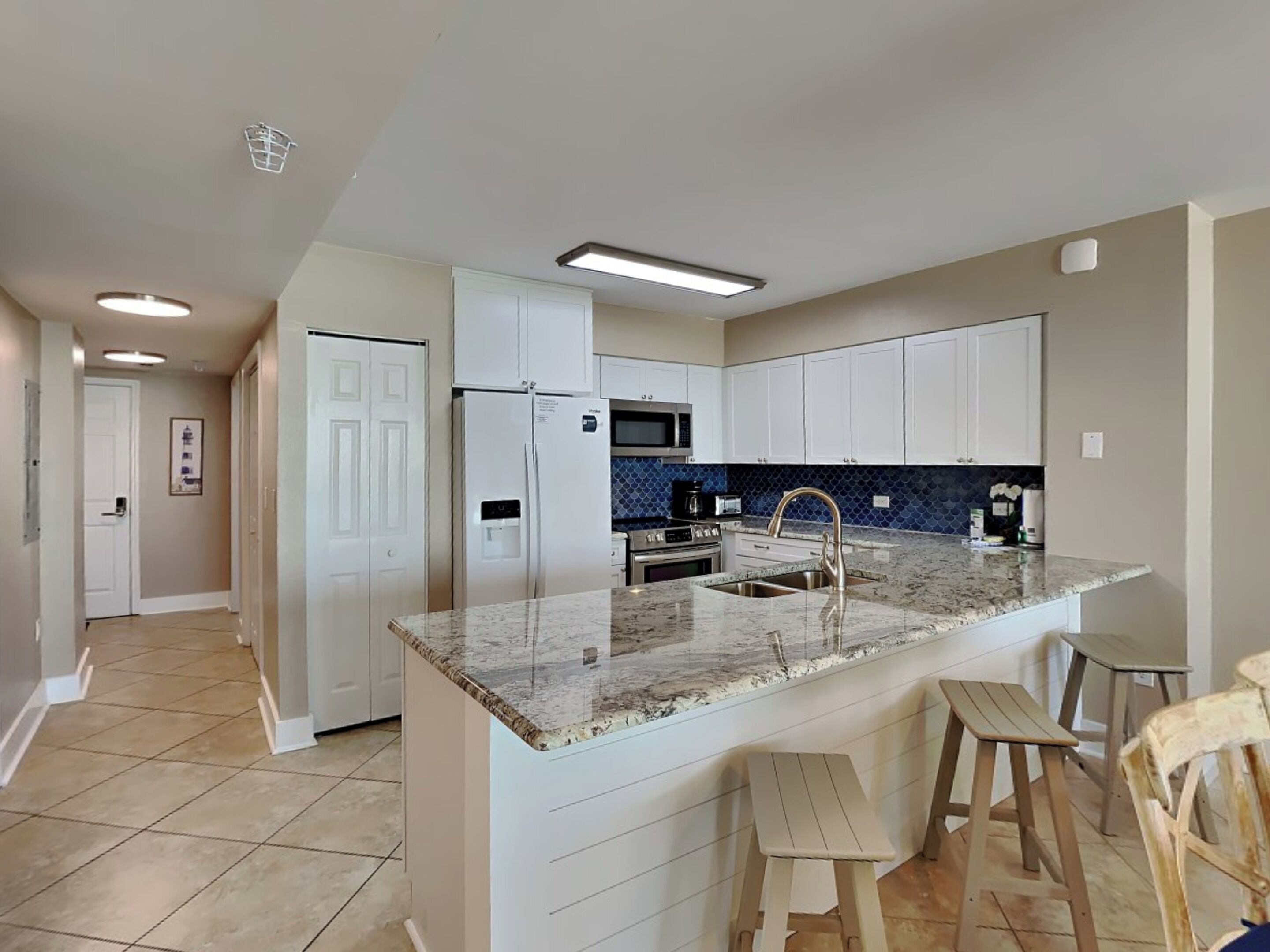 A modern kitchen with white cabinets, a granite countertop, stainless steel appliances, and a tiled floor.