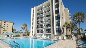 A hotel with a pool area, multiple balconies, and palm trees. - Emerald Isle #300 | Balcony Views, Pool Access, Near Area Dining & Fun! (Fort Walton Beach)