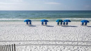A beach with white sand and a row of blue beach umbrellas. - Emerald Isle #300 | Balcony Views, Pool Access, Near Area Dining & Fun! (Fort Walton Beach)