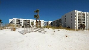 A beachfront hotel with multiple floors, a sandy beach in front, and a palm tree. - Emerald Isle #300 | Balcony Views, Pool Access, Near Area Dining & Fun! (Fort Walton Beach)