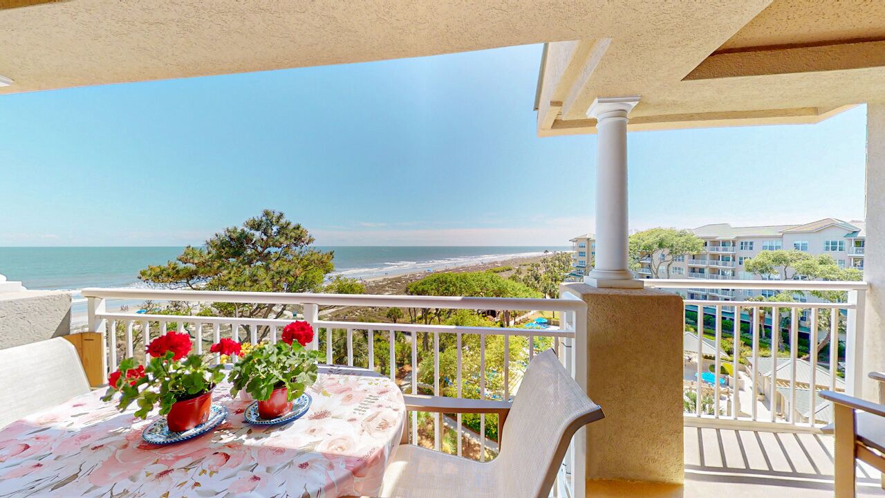 A balcony with a table and chairs, overlooking a beach and ocean.