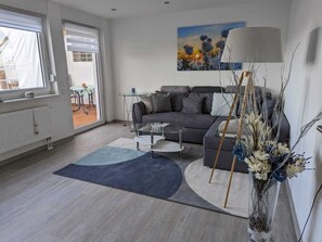 Una sala de estar moderna con un sofá gris, una mesa de centro de cristal y un ventanal grande.