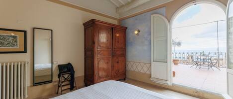 Een slaapkamer met een groot bed, een houten garderobe, een radiator, een spiegel en uitzicht op een balkon met buitenmeubilair.