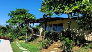 Une maison dotée d’un patio couvert, entourée d’une pelouse bien entretenue et de diverses plantes.