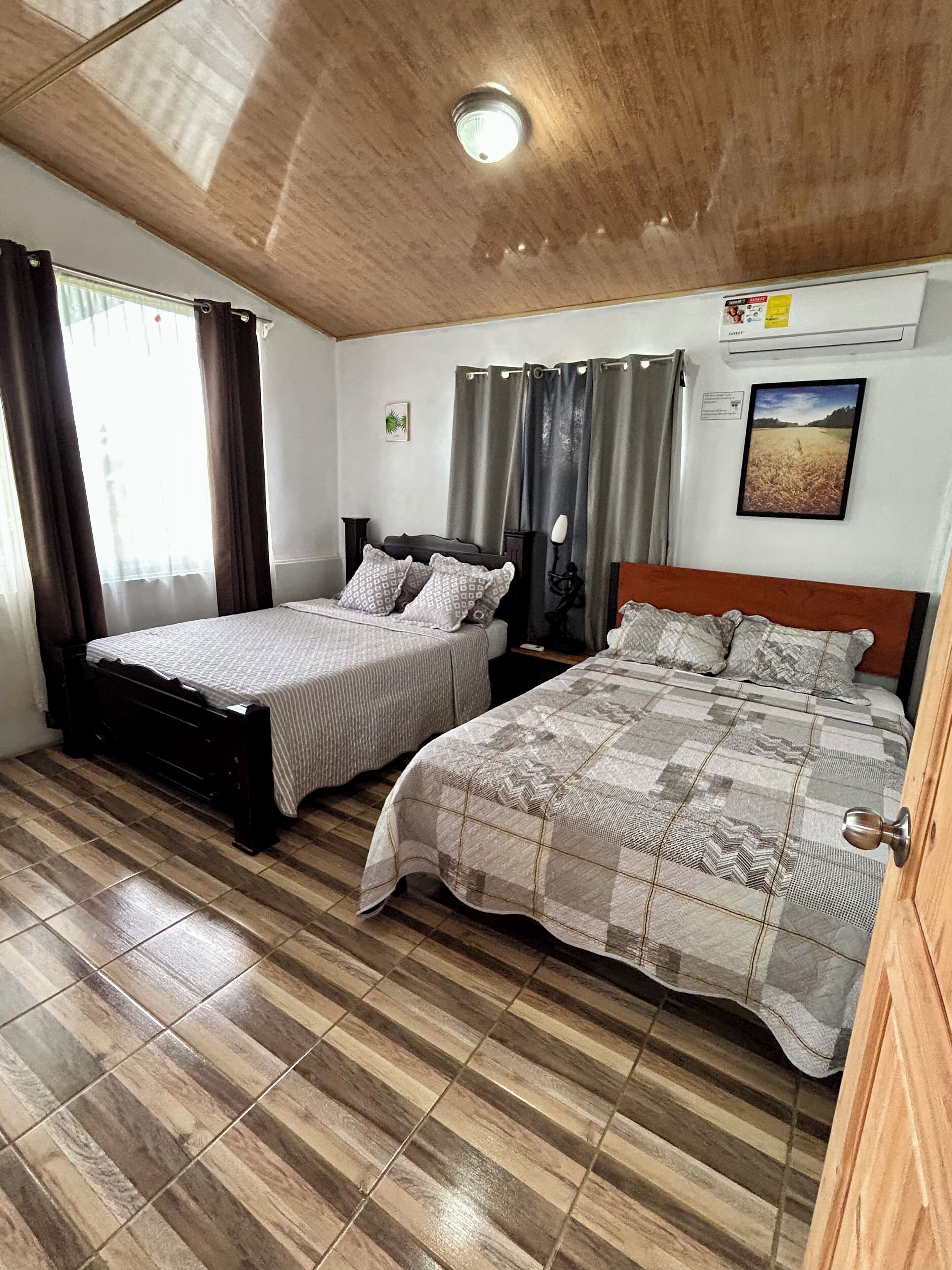 Une chambre avec deux lits, un plafond en bois, une fenêtre avec des rideaux et un climatiseur fixé au mur.