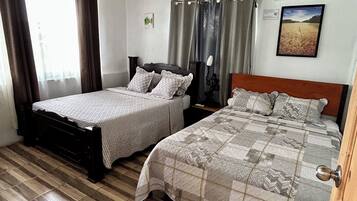 Une chambre avec deux lits, un plafond en bois, une fenêtre avec des rideaux et un climatiseur fixé au mur.