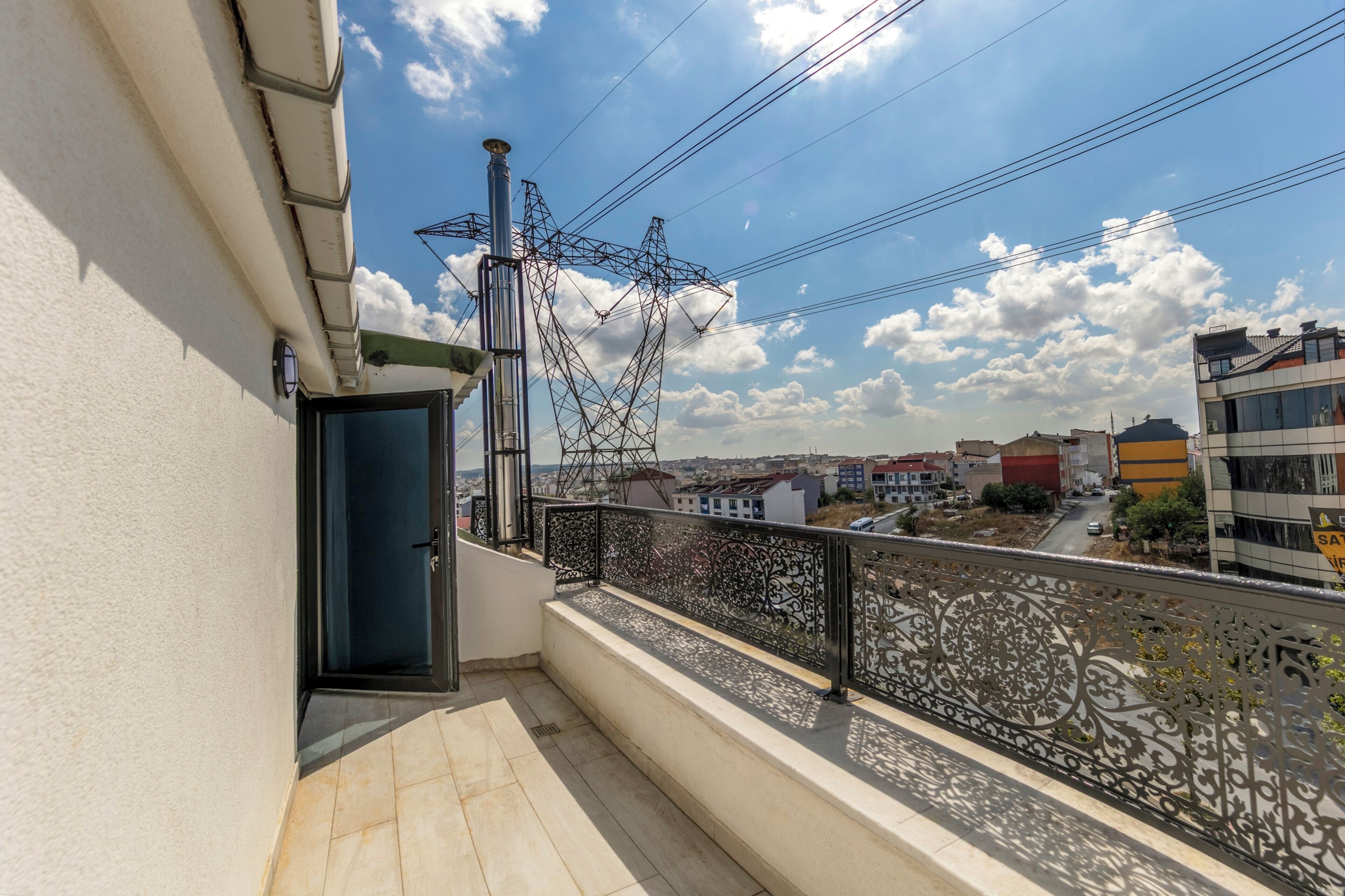 A balcony with a metal railing, a door, and a view of a cityscape with buildings and power lines.