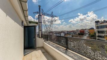 A balcony with a metal railing, a door, and a view of a cityscape with buildings and power lines.