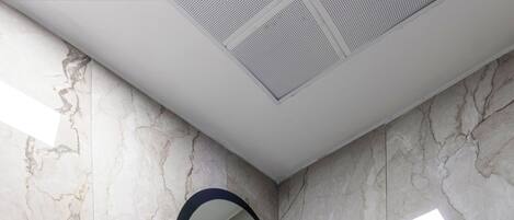 A modern bathroom with a marble wall, a round mirror, a sink, a towel rack, and a hairdryer.