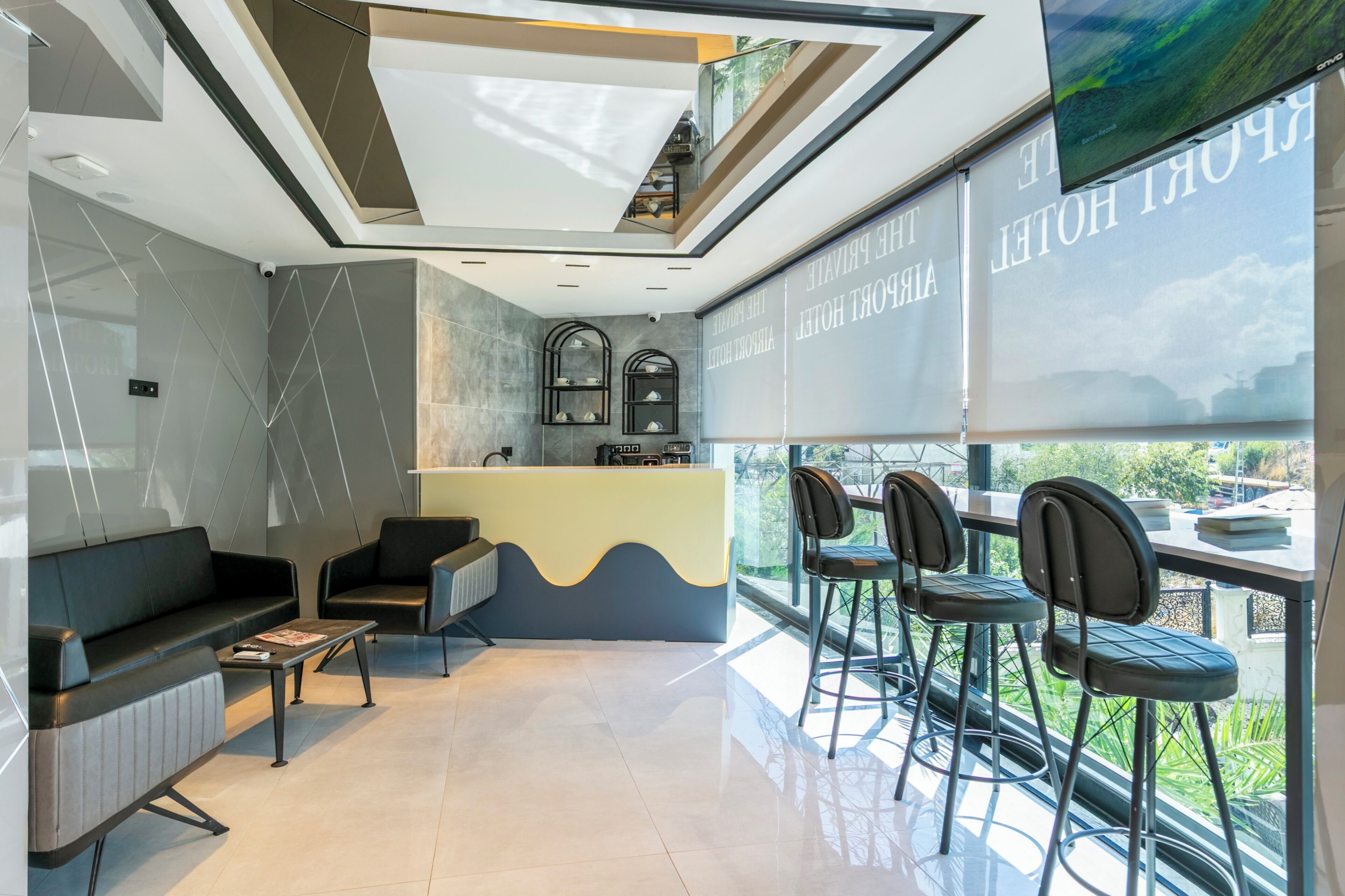 A modern hotel lobby with a reception desk, seating area, and large windows offering a view of the outdoors.