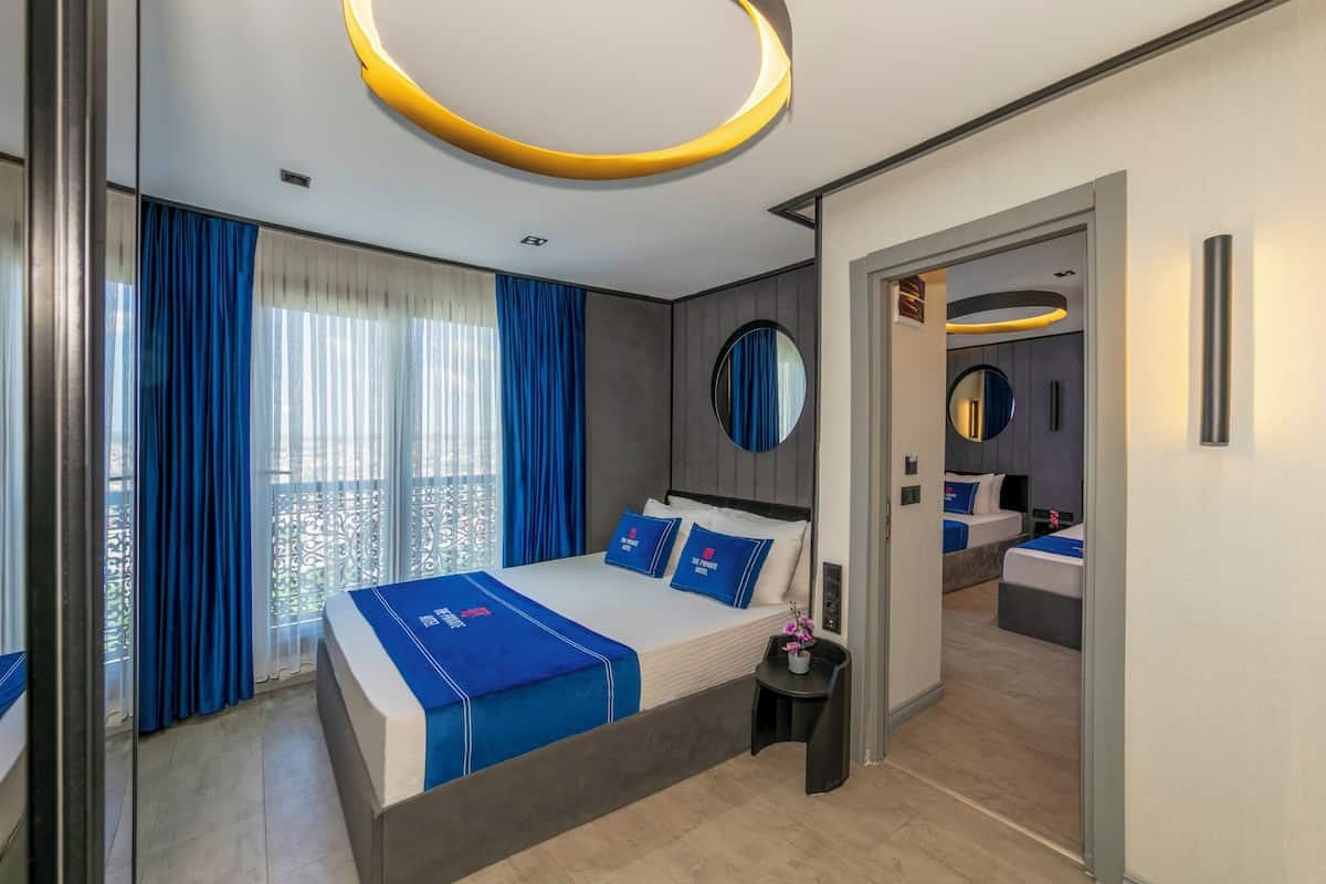 A modern hotel room with a large bed, a small side table, a mirror, and a view of the balcony.